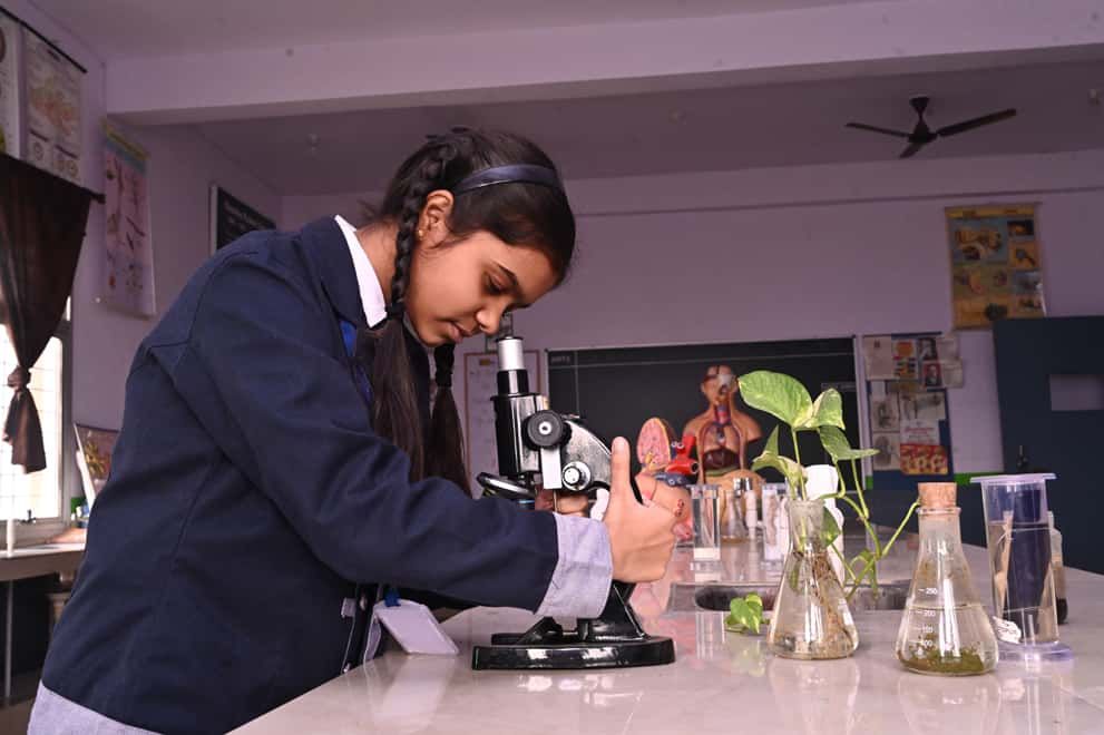 A student of Sunbeam School Ballia using a microscope beside plant specimens in flasks