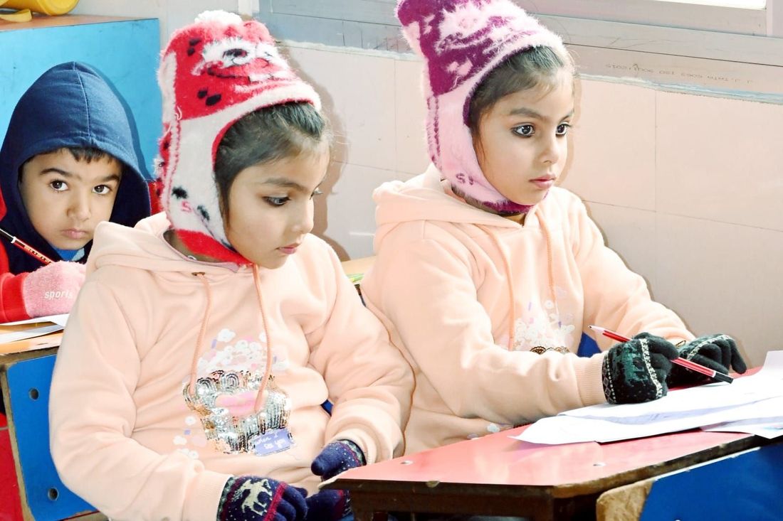 Two young children of Sunbeam School Ballia in woollen caps writing at a classroom desk