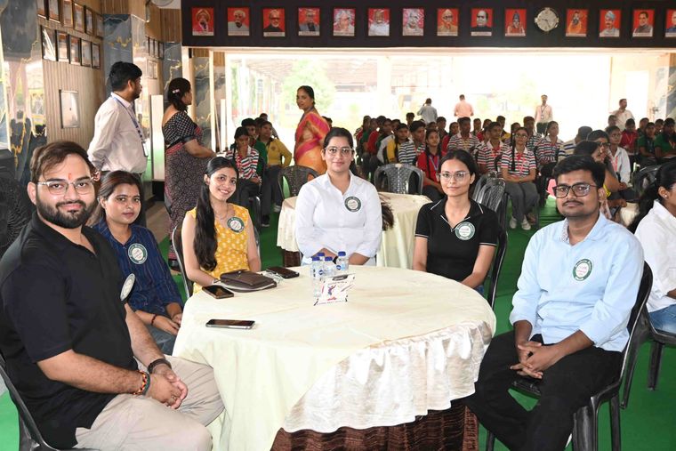 Six alumni of Sunbeam School Ballia seated at a round table in their Pradiptam badges, students of the school in rows behind them.