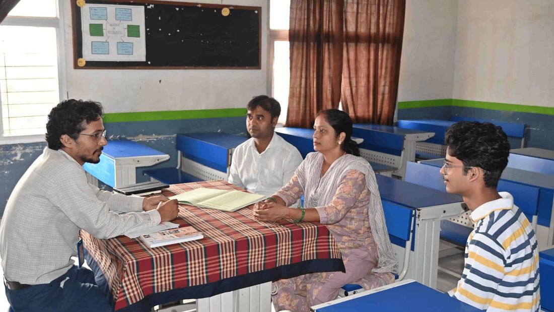A class teacher at Sunbeam School Ballia going through a student's record with both parents across the desk, the student sitting beside them