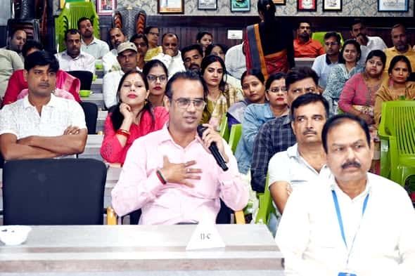 A parent speaking into a microphone during a Parents’ Forum session at Sunbeam School Ballia, class nameplates on the desks.