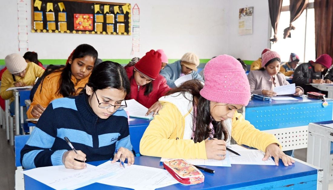 A classroom of students at Sunbeam School Ballia writing at their desks during a Parent's Orientation Programme, in coats and woollen caps
