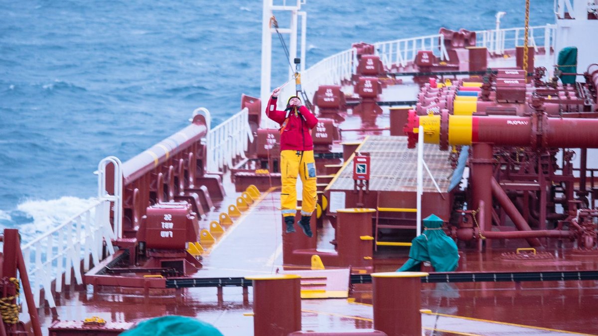 Seafaring crew operating on deck of cargo ship amidst ocean, showcasing teamwork and maritime expertise.