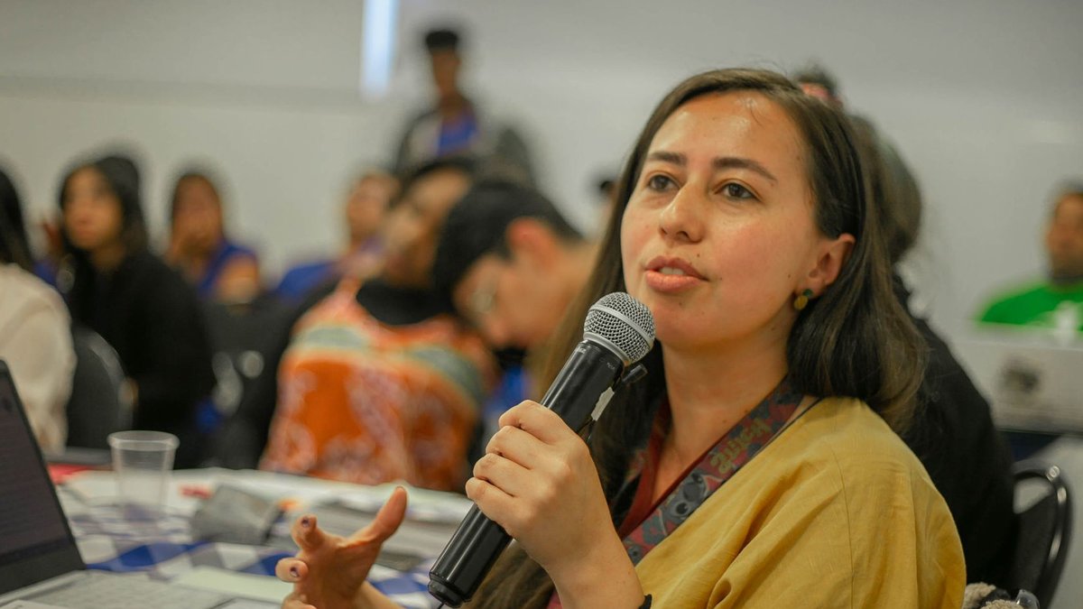Young woman with microphone speaking during a classroom presentation with students.