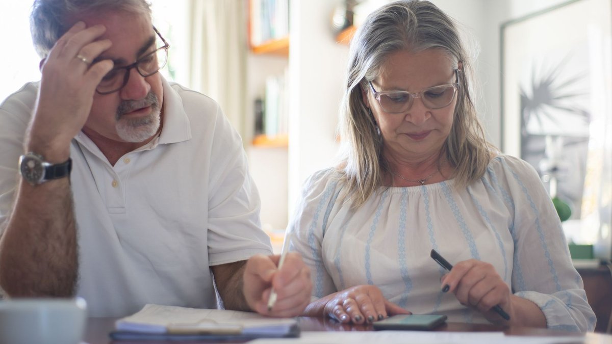 Senior couple calculating expenses at home office desk with documents and notes.