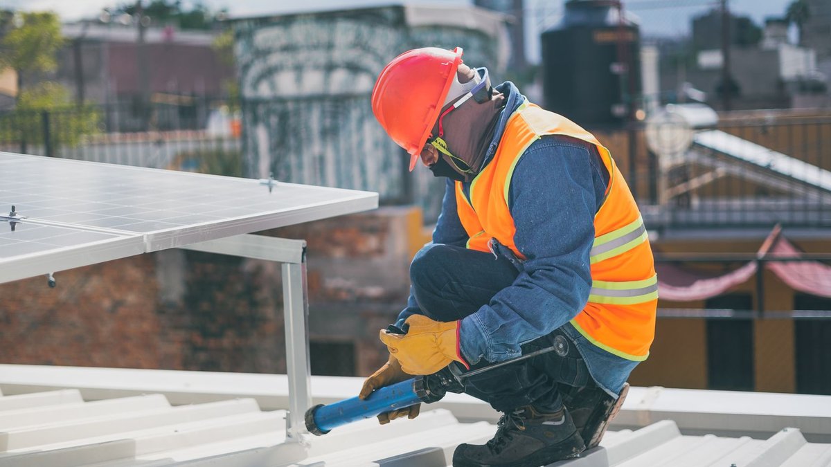 Technician in safety gear installing solar panels on a rooftop, ensuring energy efficiency.
