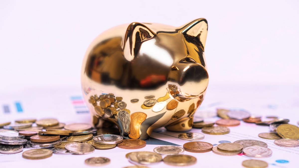 Shiny golden piggy bank on financial documents with scattered coins symbolizes savings.