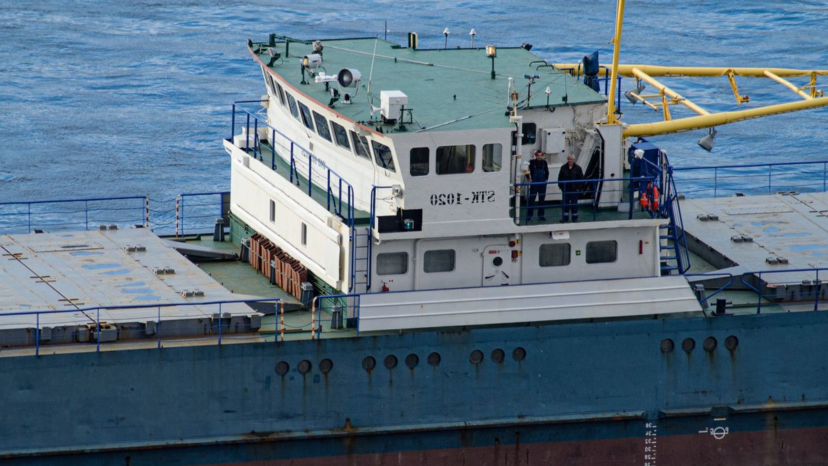 Close-up view of cargo ship with crew at the helm, navigating open blue waters.