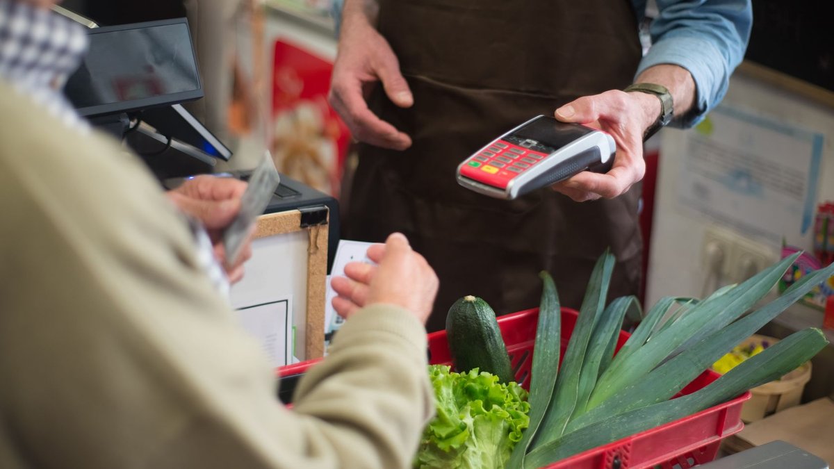 Close-up of customer paying for groceries with produce at a store checkout counter.