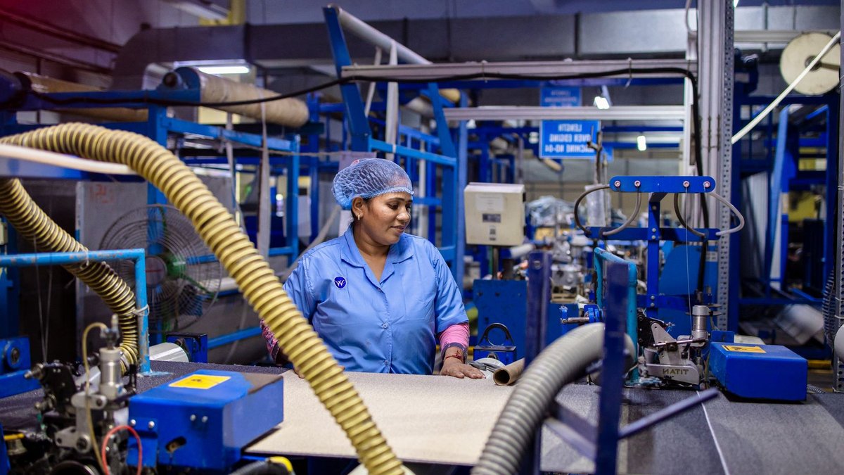 A female worker in a blue uniform operates machinery in a textile factory.