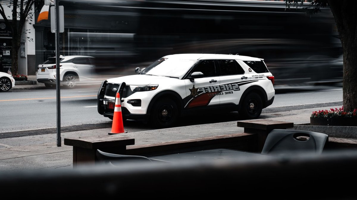 ICE Raids Terrorize NYC Kids, Sparking Community Fear Sheriff's vehicle parked on a bustling city street with traffic motion blur.