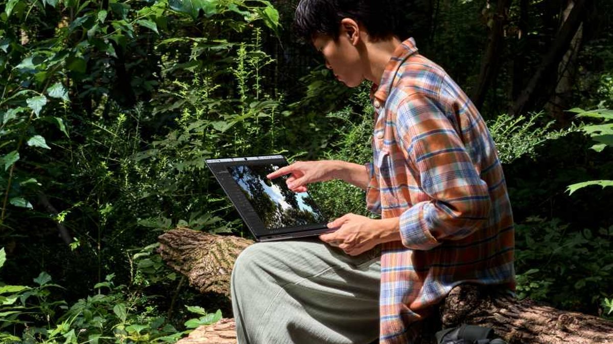 Apple Unveils Touch Screen MacBook Pro A person sits on a log outdoors using a Mac,.