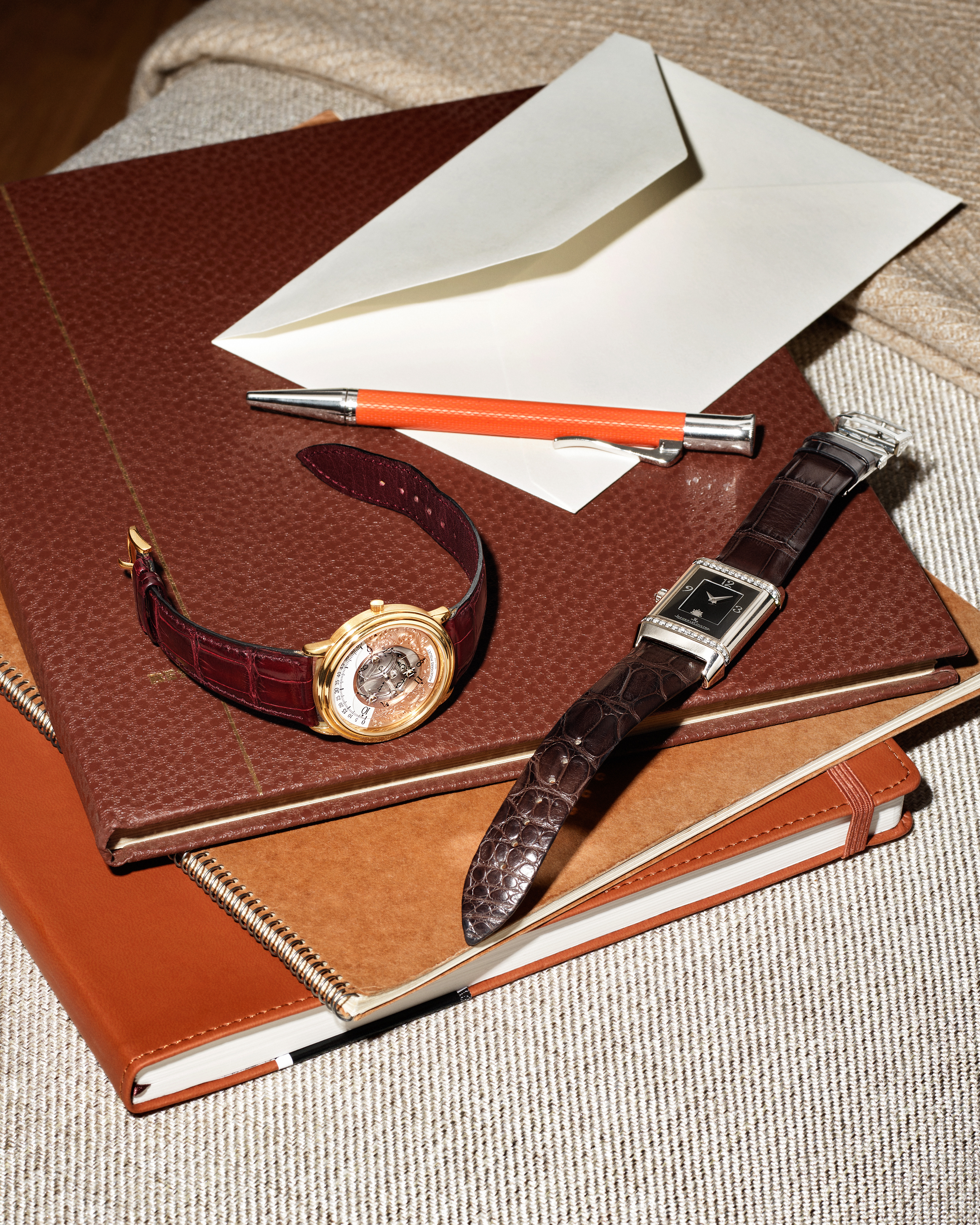 Two luxury watches displayed on a notepad with a vintage feather quill. One watch features a round skeleton dial with a black leather strap, while the other has a rectangular dial with a brown leather strap. The elegant composition emphasizes the fine craftsmanship of the timepieces.