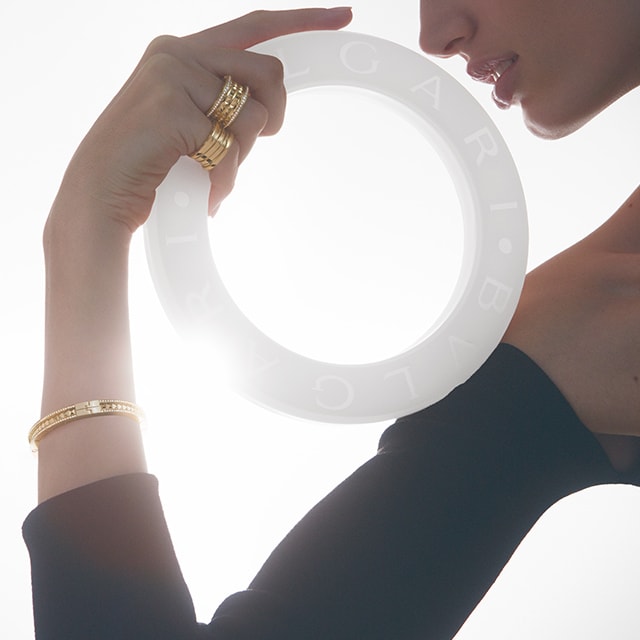 Model from the side holding a white circle with Bulgari logo and wearing B.zero1 jewellery, close up.