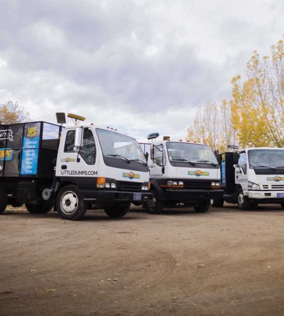 A photo of several Little Dumps dump trucks parked in a dirt lot on a cloudy day.