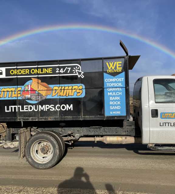A photo of a Little Dumps dump truck parked under a rainbow in the Bitterroot Valley.