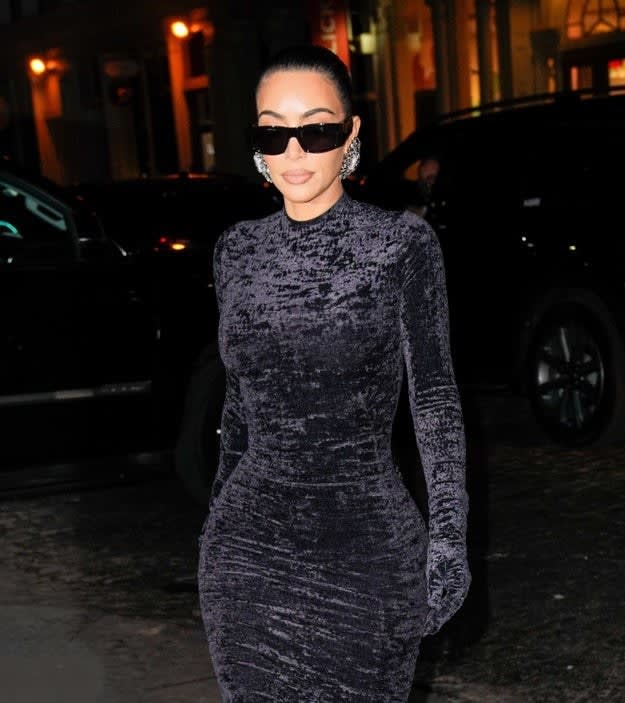 Kim walking outside at night wearing a velvet long-sleeved dress and sunglasses