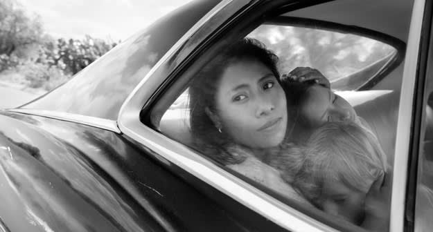 Yalitza Aparicio holding the head of two kids as she looks out the back car door window