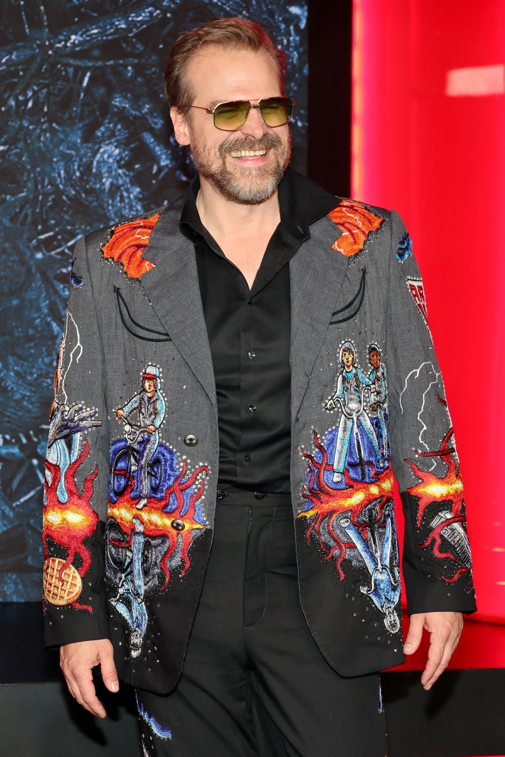David Harbour laughing with an embroidered blazer on at an event