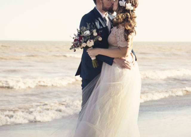 bride and groom standing beside shoreline