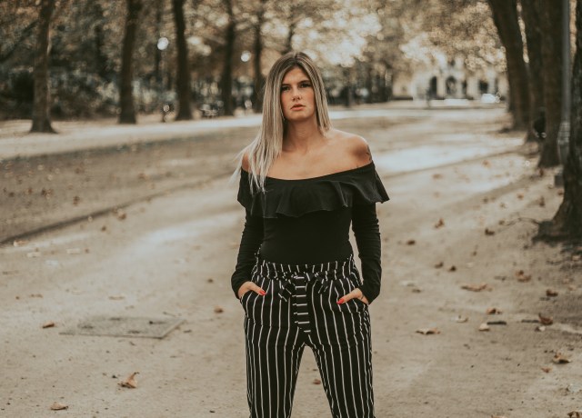 woman in black off-shoulder blouse with hands on pocket while standing near trees