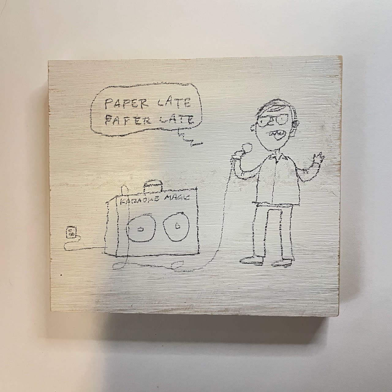 Cartoon by David Rhoden of man singing Genesis' "Paperlate" on an imaginary home karaoke machine. Cartoon is on a piece of painted plywood.