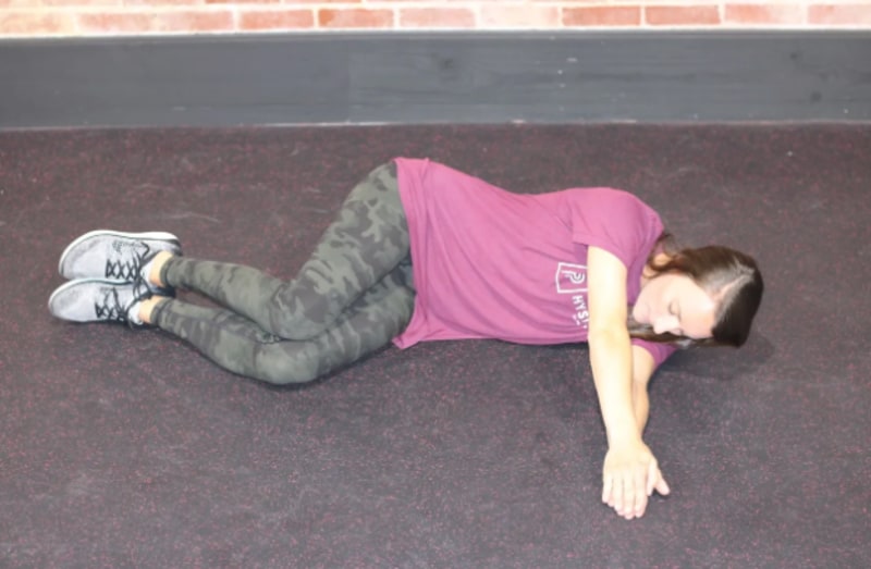 Woman lying sideways on the floor and putting her hands together out in front of her