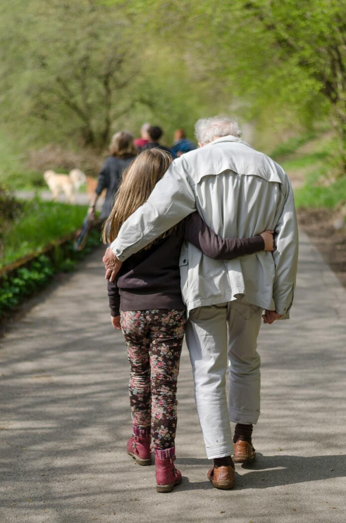 Old man and young girl walking through a park with their arms around each other