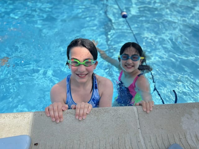 Two young Oasis Day Camp campers wearing swim goggles smiling at the edge of a bright blue pool
