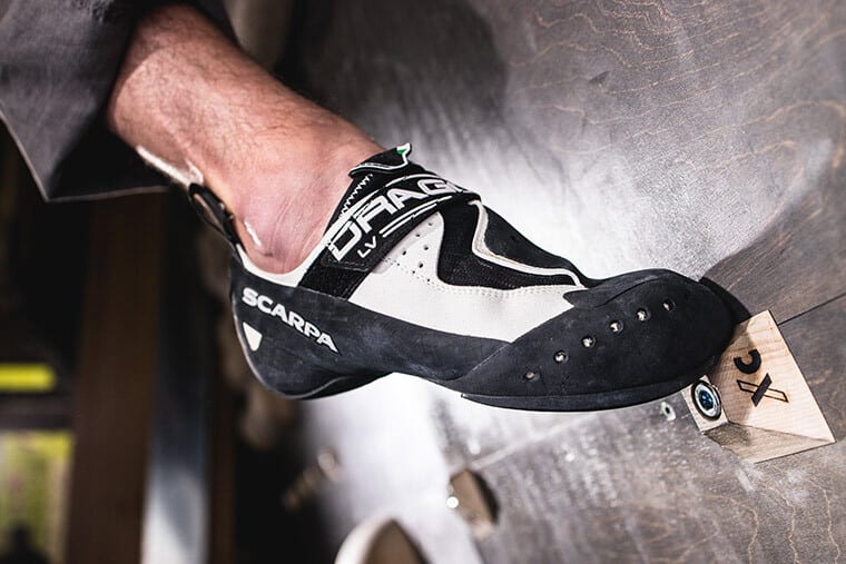 A climber wearing the Drago LV Climbing Shoe pressing down onto a wooden foot hold