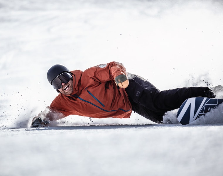 A snowboarder lays a deep toeside turn