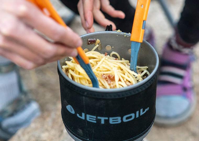 Campers mixing up spaghetti with utensils in the Jetboil MiniMo Cooking Stove