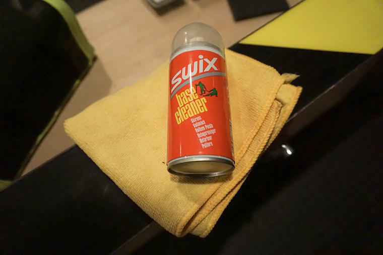 A can of Swix base cleaner and a clean rag resting on a ski base