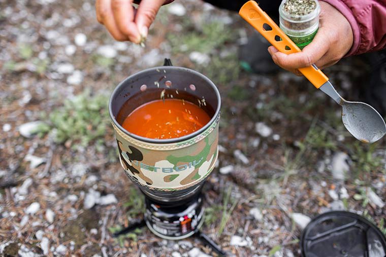 Camper adding spices to tomato soup in the Jetboil MiniMo Cooking Stove