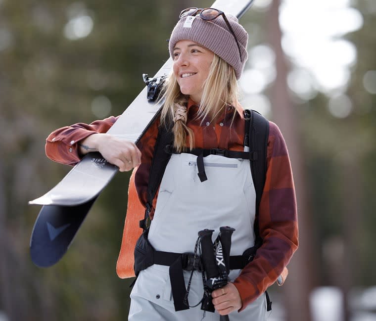 Woman carrying skis on her shoulder while wearing the Flylow Women's Foxy Bib