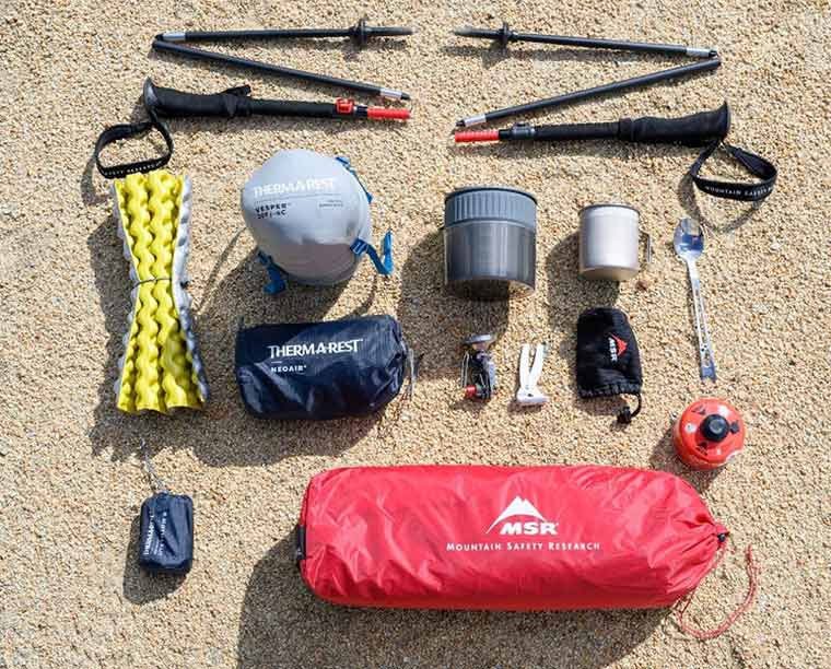 Backpacking gear laid out on the ground around the packed MSR Hubba Hubba 2 Tent