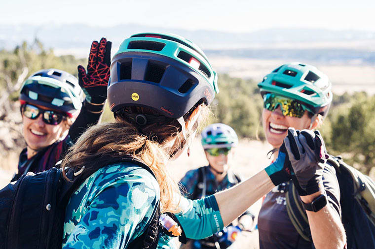 a group of women exchange high fives, while a MIPS logo is visible on the helmet in the foreground