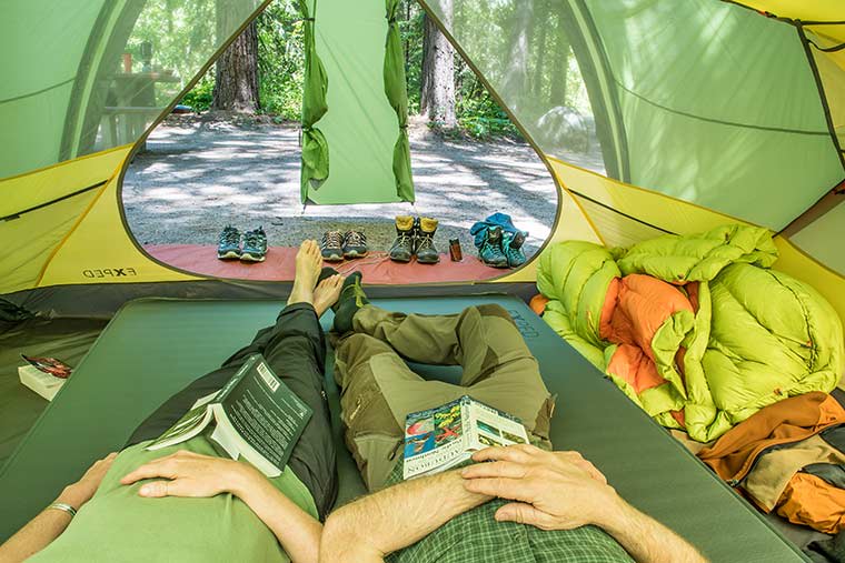 Two campers laying out on the Exped MegaMat Duo 10 Sleeping Pad inside of a tent.