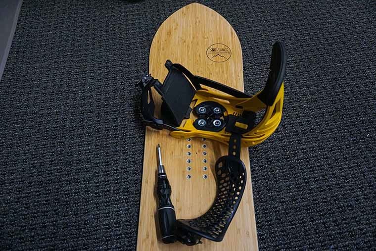 S snowboard with an unmounted binding and a screwdriver