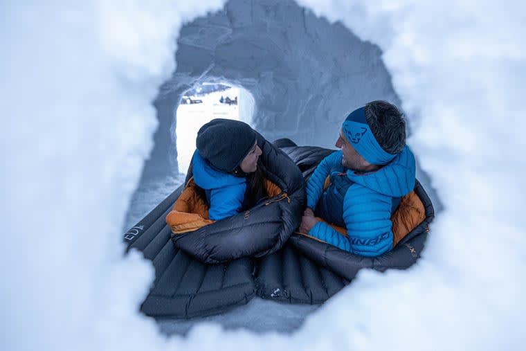 Two campers side by side in their sleeping bags inside a snow cave