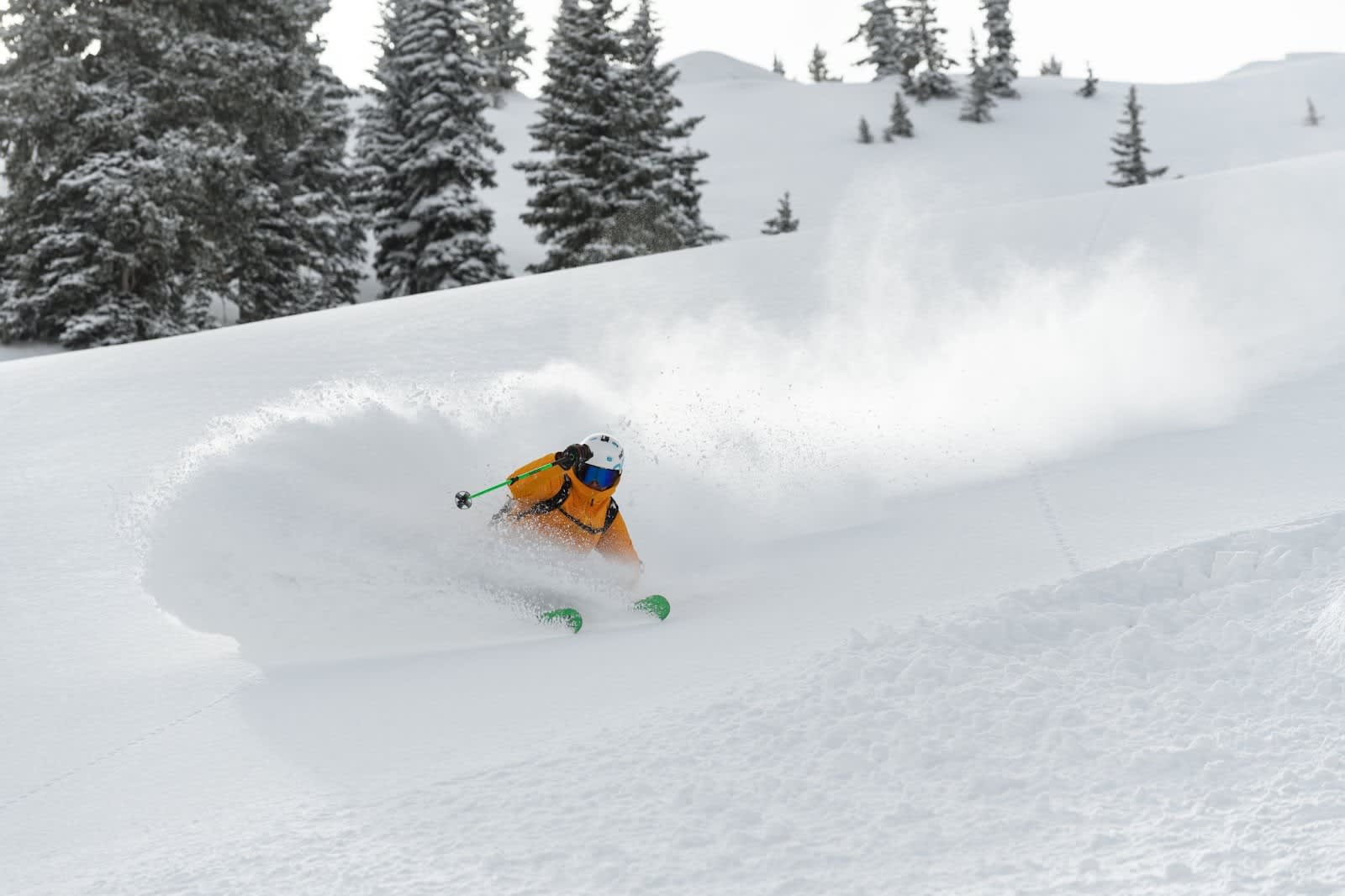 Skier in an orange jacket turning, throwing a powder cloud into the air