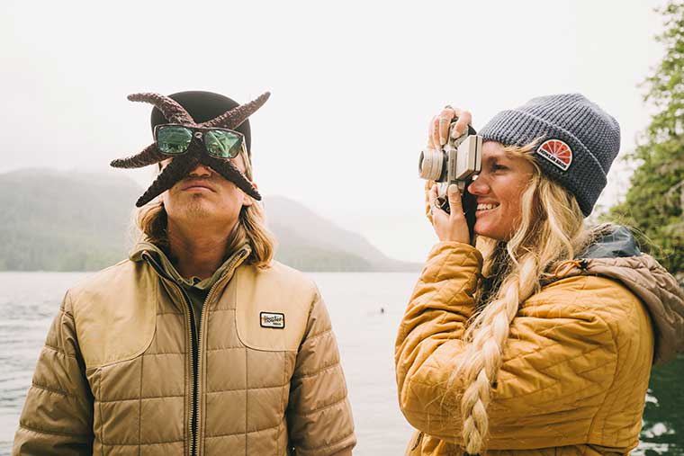 Woman taking a picture of a man with a starfish on his face wearing the Howler Bros Merlin Jacket