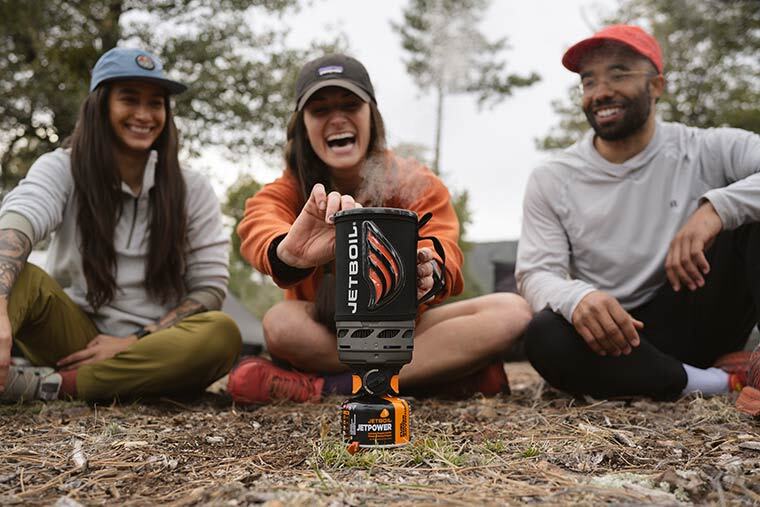 Three campers laughing whuile getting ready to remove the Jetboil Flash 1.0L cup fromt he burner