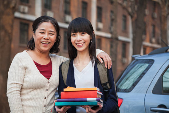 Mother and daughter portrait in front of dormitory, daughter holds a stack of books