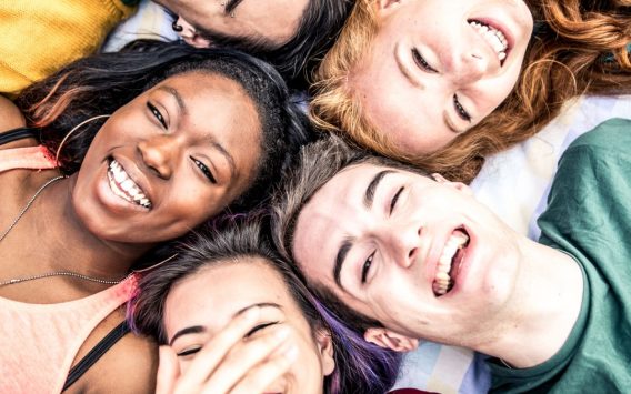 5 students lay down and look up towards the sky, laughing and smiling