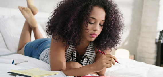 Student lounging on a bed, working on homework