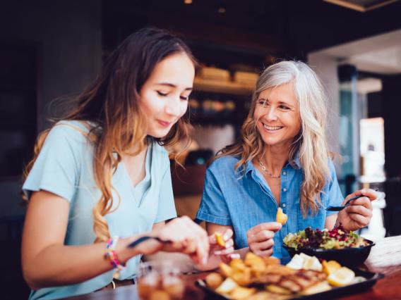 Mother and adult daughter eating lunch together and smiling.