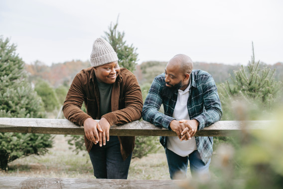 A father and son having a conversation at a tree farm, leaning over a rustic wooden fence