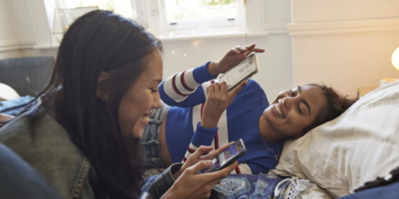 2 students lay next to each other looking at their phones