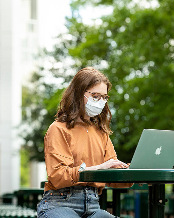 Student completing work on computer, with a mask on.